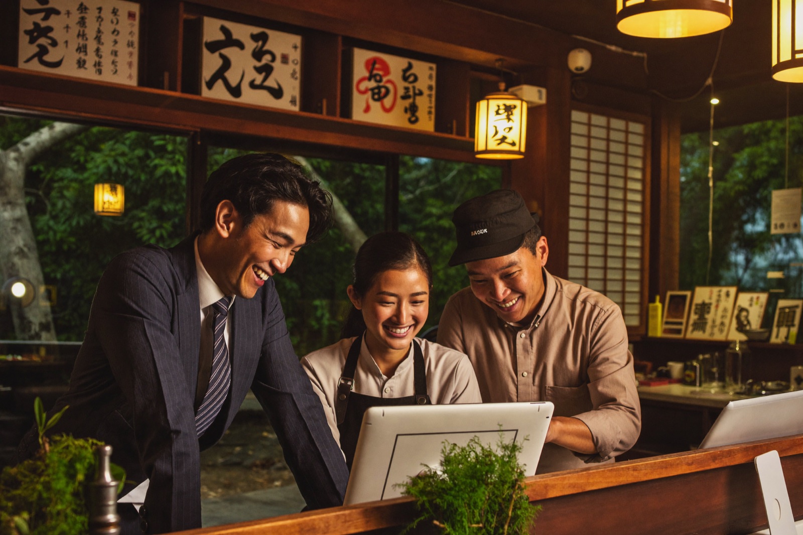 オーナーとタイ人スタッフたちがタブレット画面を見て笑い合っている様子