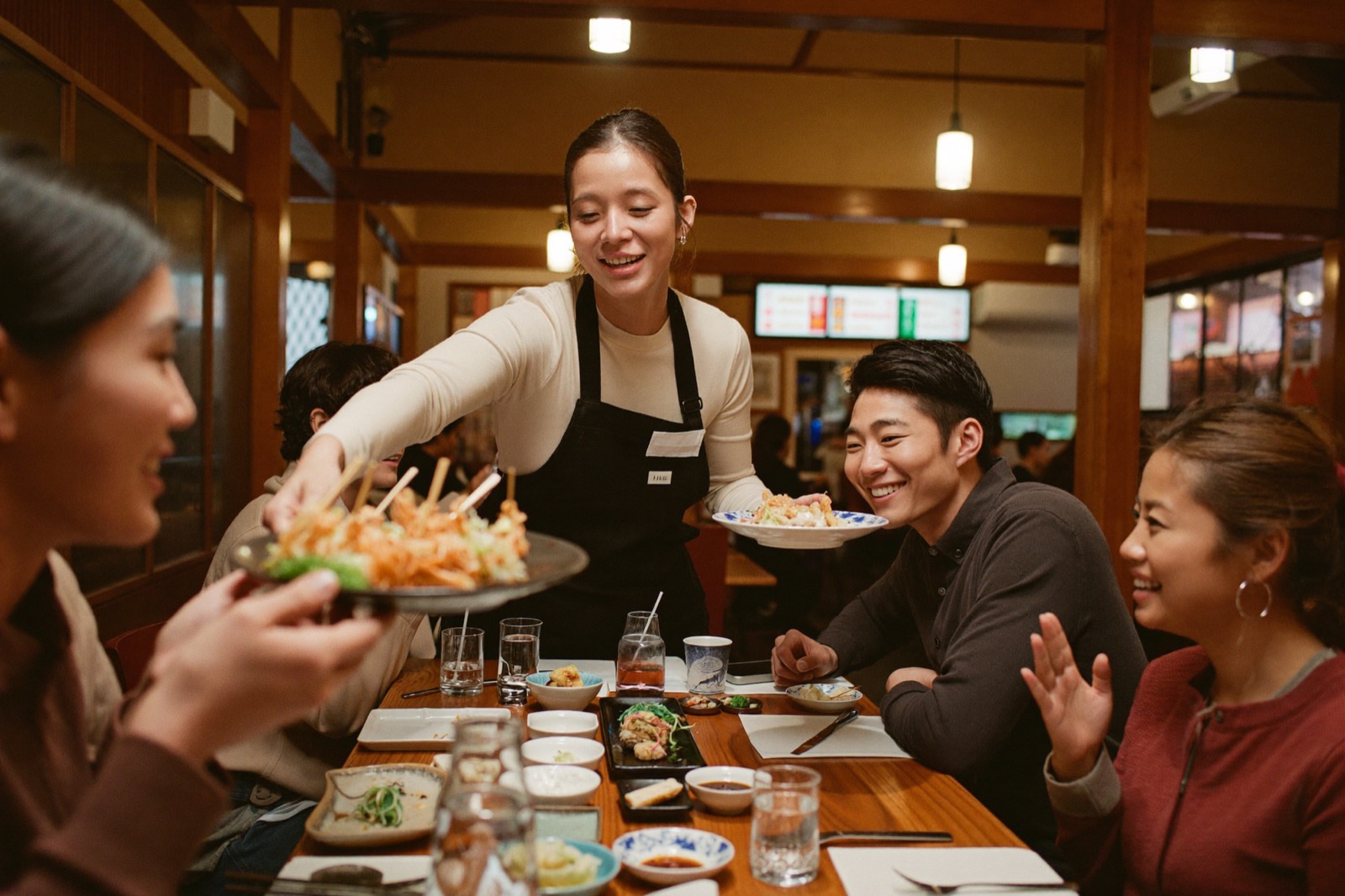 笑顔のウェイトレスが焼き鳥を配膳し、お客さんが喜んでいる店内の様子